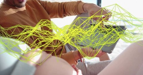 Two women lounging on bed sharing tablet with neon wireframe data overlay