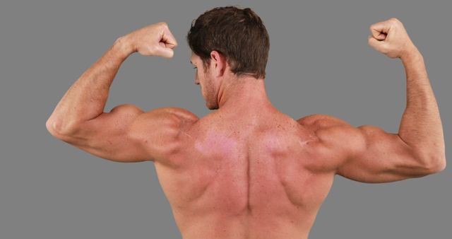 A Caucasian male bodybuilder flexes his muscles, showcasing his well-defined back and biceps, with copy space. His pose emphasizes strength and physical fitness, highlighting the results of intense training and dedication.