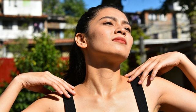 Sunlit asian woman raising hands adjusting black tank top straps backyard portrait outdoor