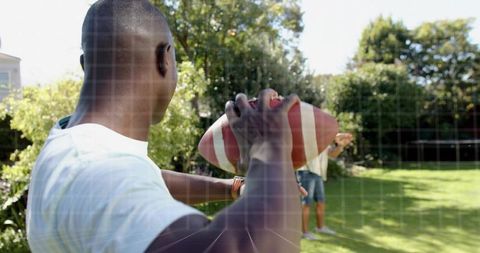 Young man preparing to throw football in sunny backyard garden with friend practicing catch