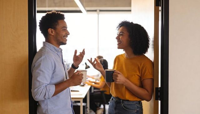 Coworkers chatting over coffee in doorway, casual workplace conversation and collaboration