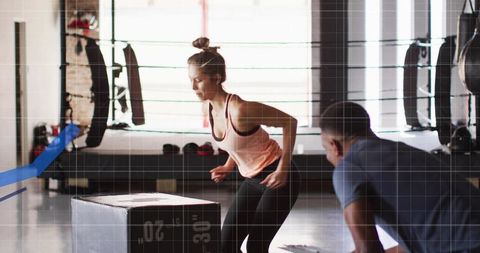 Woman performing plyo box jump in boxing gym with coach observing strength and agility