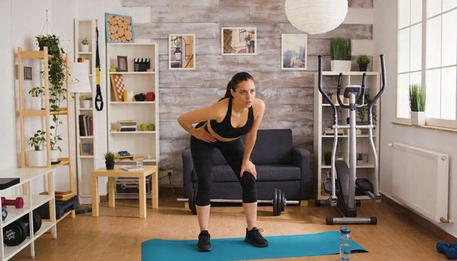 Woman leaning forward performing bending stretch on blue mat in living room gym