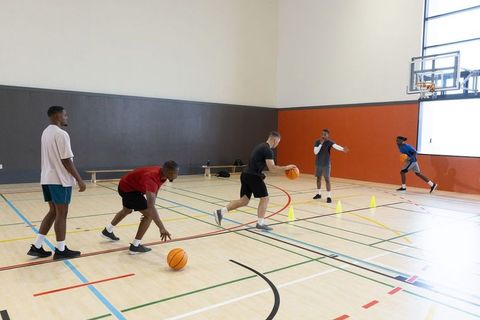 Diverse male basketball players practicing cone drills in indoor gym with coach
