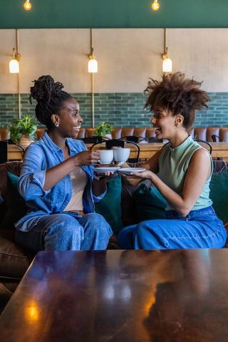 African american friends clinking coffee cups on leather sofa in cozy cafe