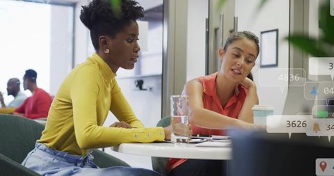 Diverse women collaborating over laptop and documents in bright modern coworking space