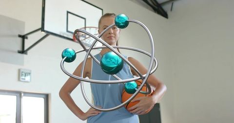 Female basketball player holding ball with levitating orbital sculpture in gym