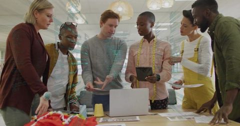 Creative diverse team collaborating in modern design studio around laptop