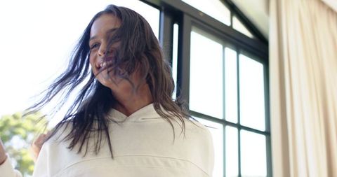 Sunlit african american woman smiling at home in white hoodie by black window windblown joy