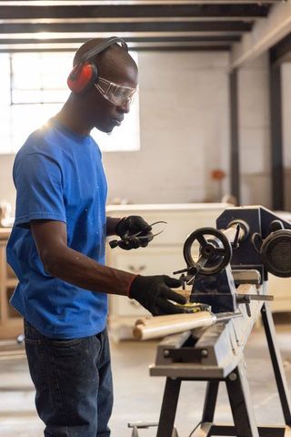 Crafting wooden spindle on lathe while wearing safety gear in carpentry workshop