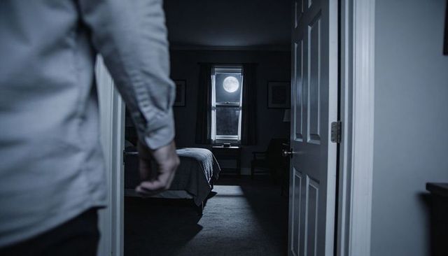 Man standing watching moonlight spilling across bed and carpet through open doorway