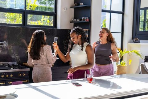 Sunlit kitchen with african american women laughing, toasting champagne
