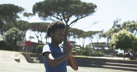 Young person meditating outdoors on park lawn practicing mindfulness and calm by playground