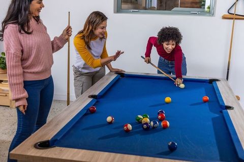 Diverse women playing pool in modern game room, lining up shot and laughing together