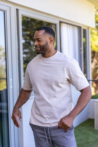 African american man standing on sunlit patio wearing beige t-shirt and gray jogger pants