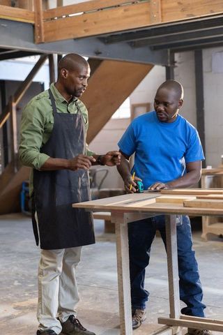 Senior mentor teaching apprentice measuring and marking wood at workshop bench