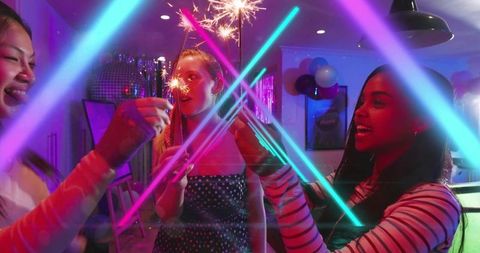 Friends celebrating with sparklers under neon lasers at indoor party with disco ball