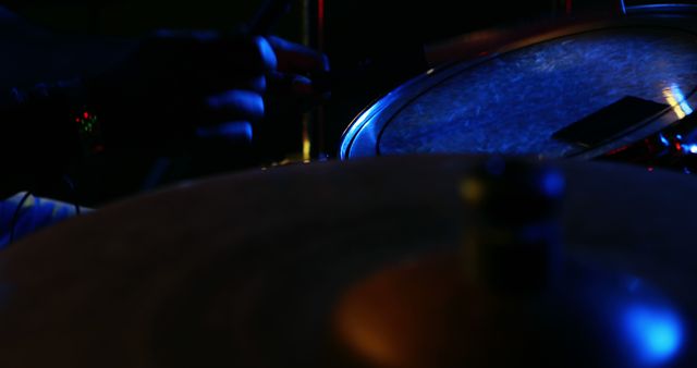 A close-up view of a drum set in low light conditions, with copy space. Visible in the frame are a cymbal and part of a drum, capturing the atmosphere of a live music performance.