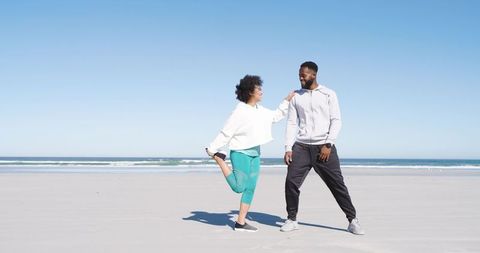 Couple stretching and balancing on beach during outdoor workout wellness routine