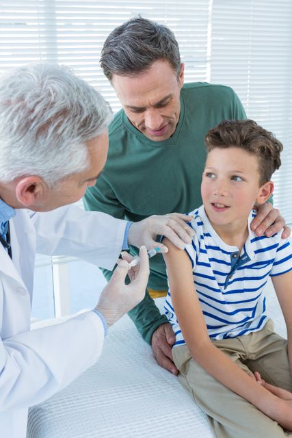 Doctor administering a vaccine to a young boy while his father supports him. Ideal for use in healthcare, medical, and family-oriented content. Can be used to promote immunization, pediatric care, and family health services.