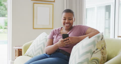 Smiling Woman Relaxing on Sofa Engaging with Smartphone