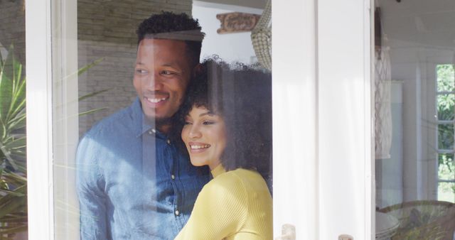 Young couple smiling and embracing while standing by home window. Showcases love, affection, and intimacy. Ideal for promoting lifestyle content, relationship tips, home decor, and advertisements centered on romance and togetherness.