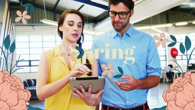 Two office colleagues interacting while standing in a modern office. They are using a tablet device for collaborative work. Spring-themed floral decorations and the word 'Spring' are creatively overlaid on the scene, adding a touch of seasonal cheerfulness. This can be used for presentations on modern workplace culture, teamwork, spring-themed office campaigns, or business collaboration concepts.