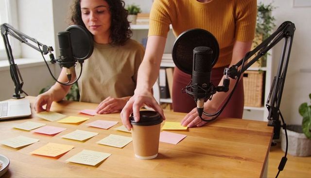 Podcast co-hosts planning episode with sticky notes and microphones in home studio