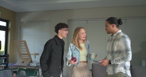 Diverse team chatting in modern home office holding phone and travel mug