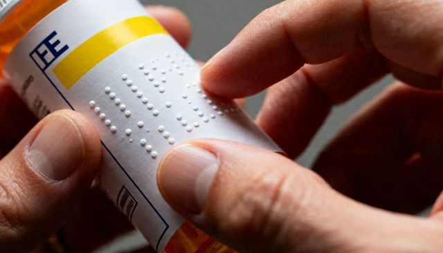 Hands reading braille medication label on prescription bottle for accessibility