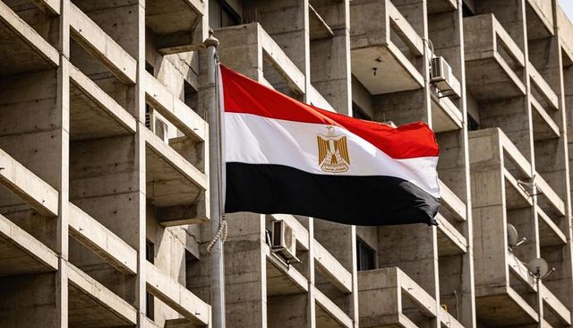 Egyptian flag fluttering over concrete apartment block with balconies and ac units
