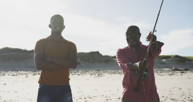 African american senior father and adult son standing on a beach fishing and talking. healthy outdoor family leisure time together.