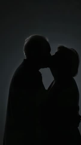 Vertical video of senior couple pressing foreheads and kissing in tender backlit silhouette