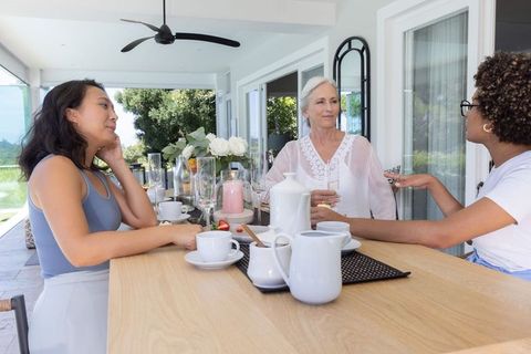Multigenerational women sipping tea and chatting on sunny veranda with porcelain tea set