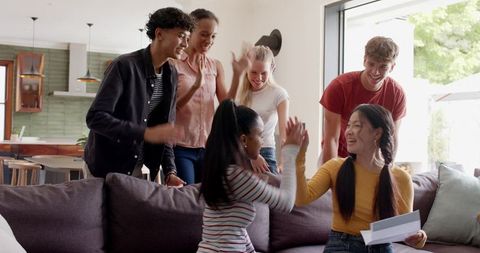 Diverse young friends celebrating with high five around sofa in bright modern living room