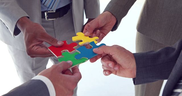 Diverse business professionals collaborate to fit puzzle pieces together, symbolizing teamwork and problem-solving. Their cooperation highlights the importance of unity in achieving common goals in the corporate world.