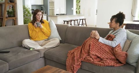 Friends enjoying coffee and conversation on cozy gray sectional with warm blanket