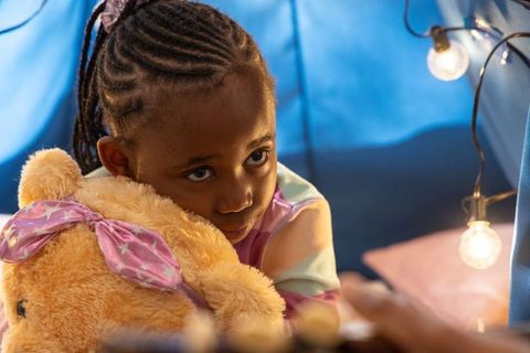 African american girl hugging teddy bear in cozy blue fort with glowing string lights