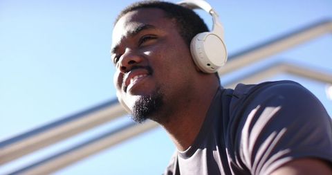 African American Man Listening to Music with Headphones Outdoors on Sunny Blue Sky
