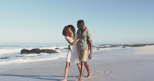 Happy diverse couple embracing and talking, walking on sunny beach by the sea. Summer, free time, relaxation, romance and vacations.