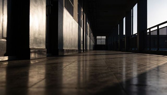Empty corridor leading to distant window with reflective tiled floor and strong shadows