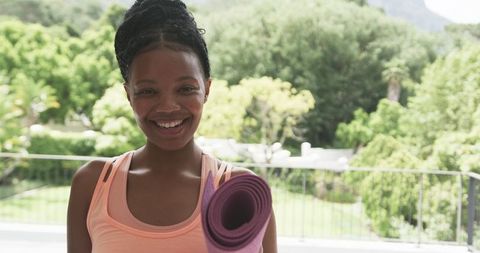 Smiling Woman with Yoga Mat in Serene Outdoor Garden