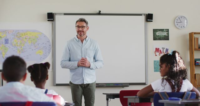 Portrait of happy caucasian male teacher in classroom with children during lesson. children in primary school.