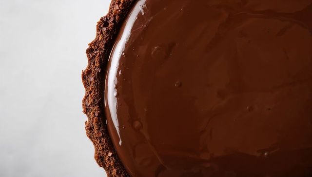 Glazed chocolate ganache tart with crunchy crumb crust close-up over pale countertop