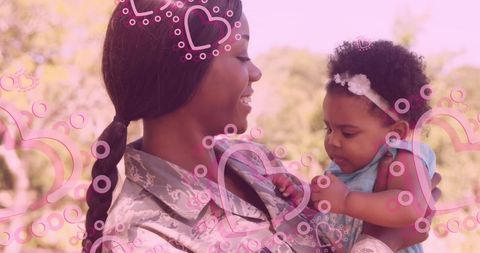 Smiling female soldier holding baby outdoors