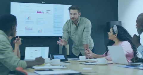 Manager presenting data on large screen in modern boardroom, team collaborating around table