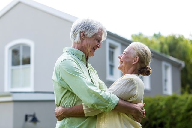 Smiling senior couple embracing in yard against house