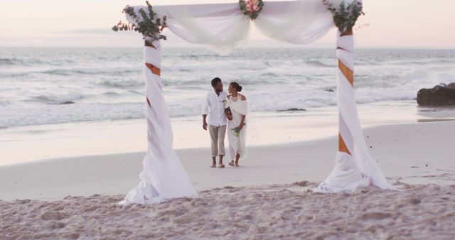 Romantic couple holding hands during wedding ceremony on beach at sunset. Can be used for wedding invitations, romantic getaway promotions, or travel advertisements.