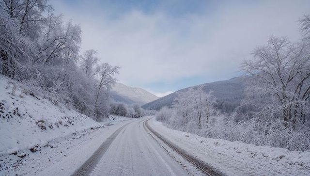 Curving snow-covered road winding through frosted mountain valley with tire tracks