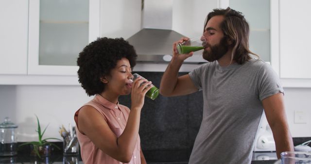 Couple drinking green smoothies in a modern kitchen, promoting a health-conscious lifestyle. Ideal for advertisements on healthy living, wellness blogs, and nutrition product promotions.